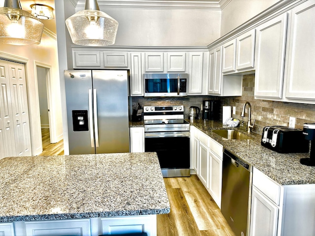 kitchen featuring pendant lighting, crown molding, stainless steel appliances, sink, and light hardwood / wood-style floors