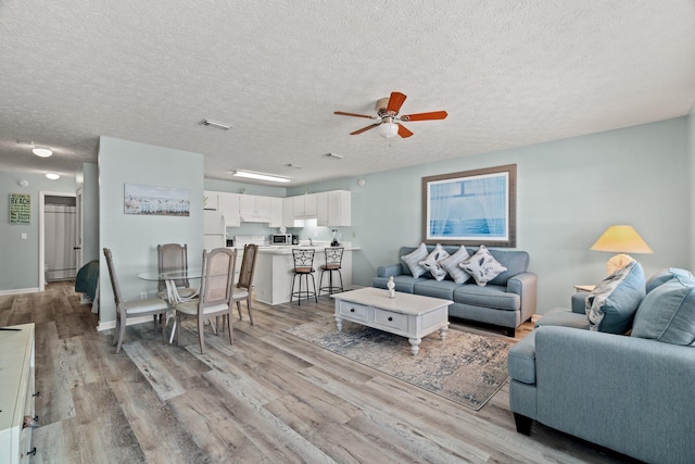 living room with light hardwood / wood-style floors, ceiling fan, and a textured ceiling