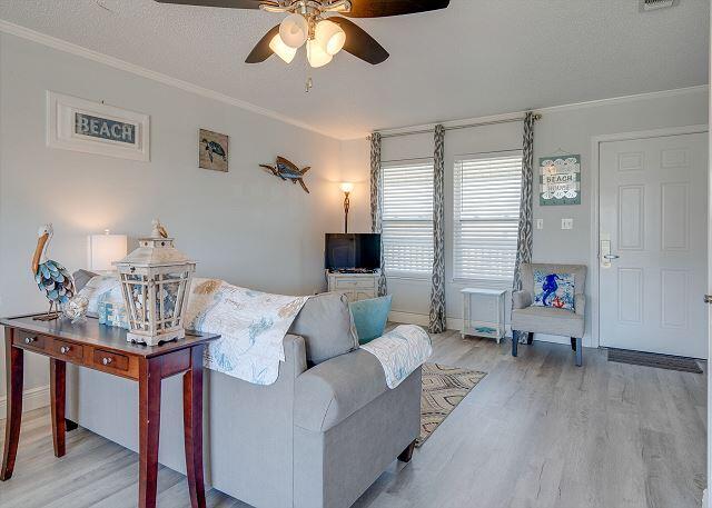 living room featuring ornamental molding, ceiling fan, light wood-type flooring, and a textured ceiling