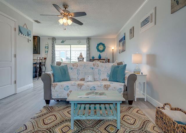 living room with ornamental molding, ceiling fan, a textured ceiling, and light wood-type flooring