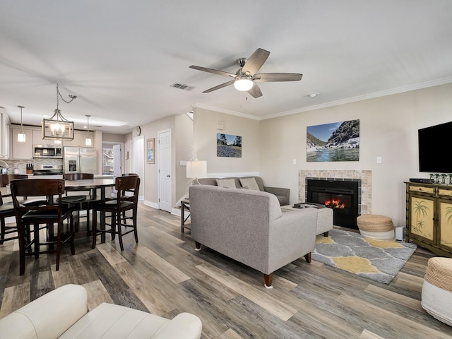 living room featuring ceiling fan with notable chandelier, a fireplace, dark hardwood / wood-style flooring, and crown molding