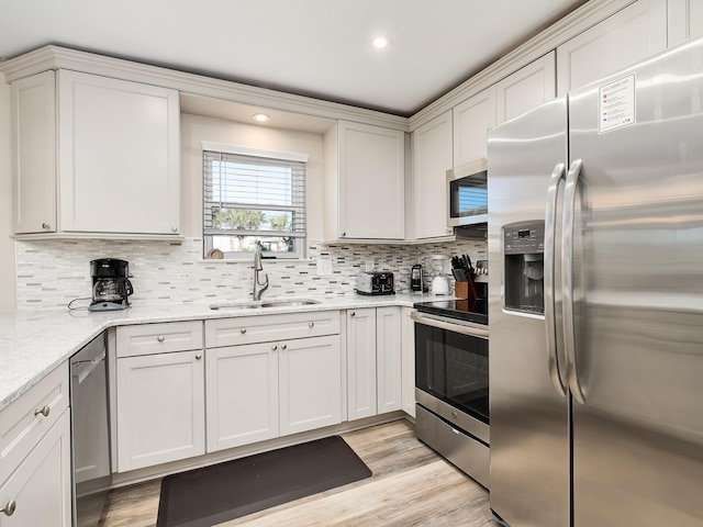 kitchen with appliances with stainless steel finishes, sink, backsplash, light hardwood / wood-style flooring, and light stone countertops