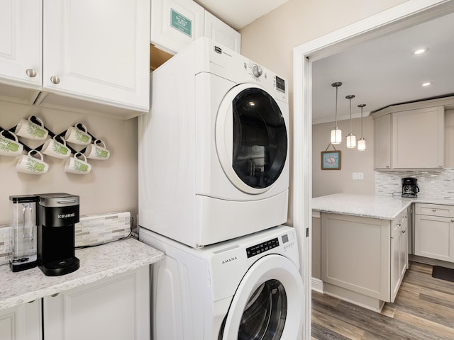 laundry area with stacked washing maching and dryer, cabinets, and hardwood / wood-style floors