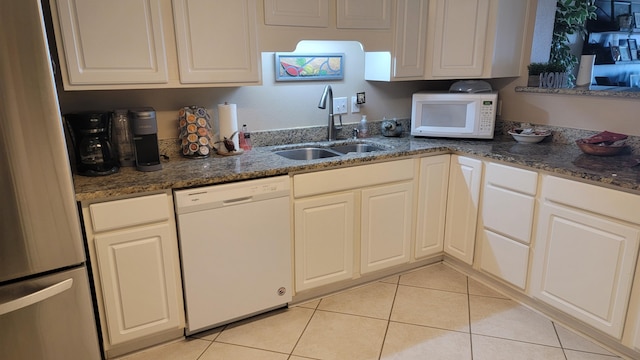 kitchen featuring white appliances, light tile patterned flooring, a sink, and dark stone countertops