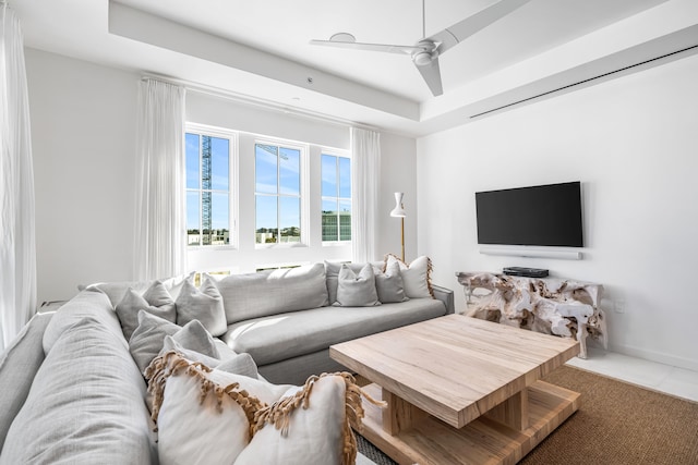 living room featuring a tray ceiling, ceiling fan, and tile floors