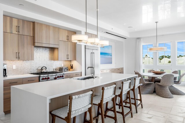 kitchen featuring hanging light fixtures, stove, a kitchen island with sink, sink, and a breakfast bar