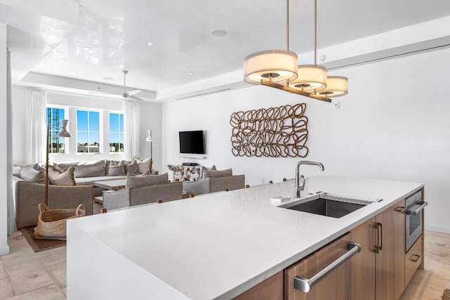 kitchen featuring decorative light fixtures, stainless steel appliances, a kitchen island with sink, sink, and a raised ceiling