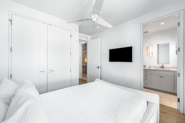 bedroom with a closet, light wood-type flooring, ensuite bath, sink, and ceiling fan