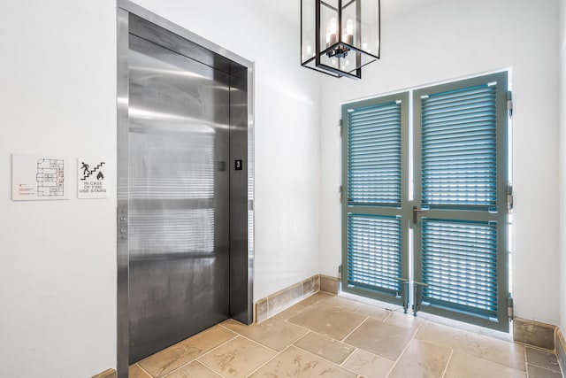 foyer with elevator, light tile floors, and an inviting chandelier