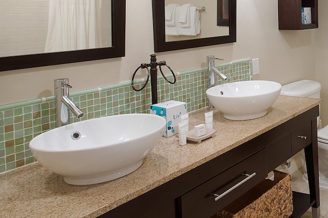 bathroom with backsplash, double vanity, toilet, and tile walls