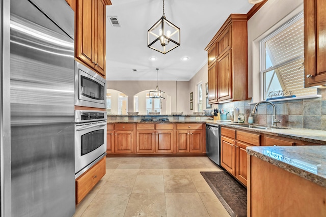 kitchen featuring sink, hanging light fixtures, a notable chandelier, built in appliances, and decorative backsplash