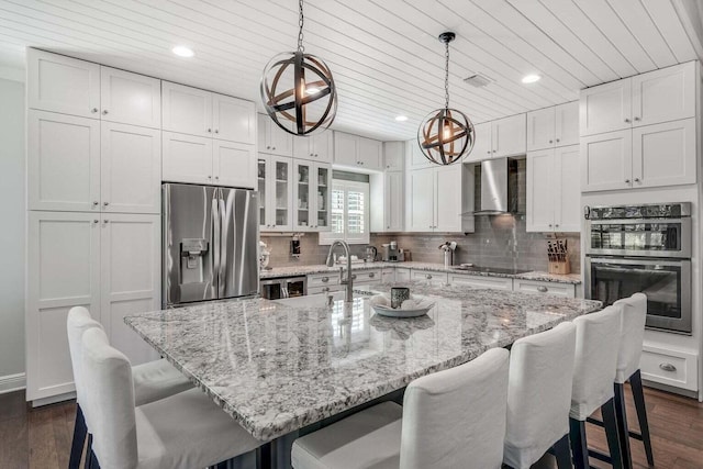 kitchen with hanging light fixtures, stainless steel appliances, a center island with sink, wall chimney range hood, and dark hardwood / wood-style flooring