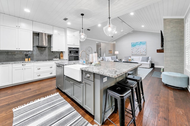 kitchen with pendant lighting, a kitchen island with sink, a breakfast bar, dark wood-type flooring, and wall chimney range hood