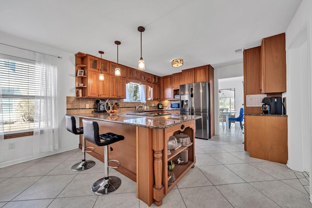 kitchen featuring decorative light fixtures, backsplash, dark stone counters, stainless steel fridge, and light tile floors