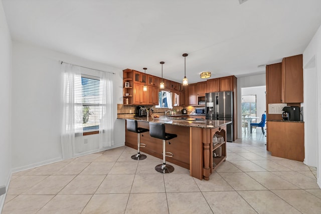 kitchen with dark stone countertops, hanging light fixtures, light tile flooring, and backsplash