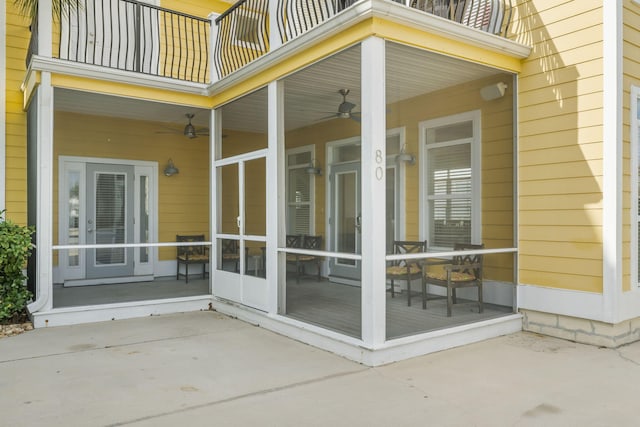 view of exterior entry with ceiling fan and a balcony