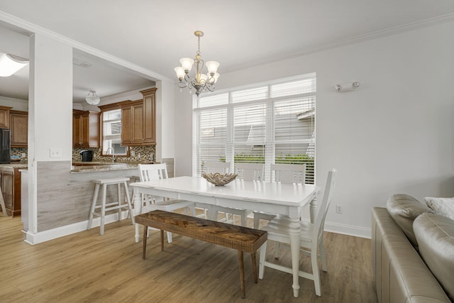 dining room with sink, light hardwood / wood-style floors, an inviting chandelier, and crown molding