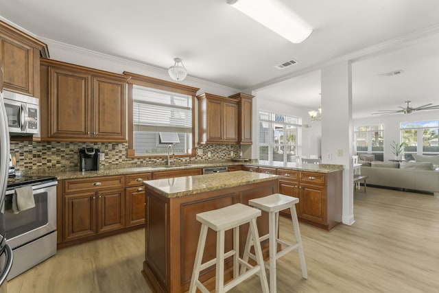 kitchen featuring appliances with stainless steel finishes, a center island, backsplash, ceiling fan with notable chandelier, and light hardwood / wood-style flooring