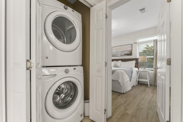 laundry area with stacked washing maching and dryer and light wood-type flooring