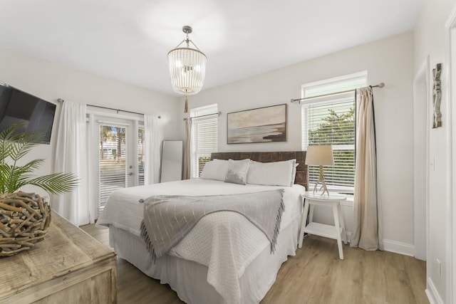 bedroom with multiple windows, light hardwood / wood-style floors, access to exterior, and a chandelier