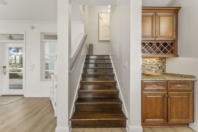 staircase with crown molding, light wood-type flooring, and indoor bar