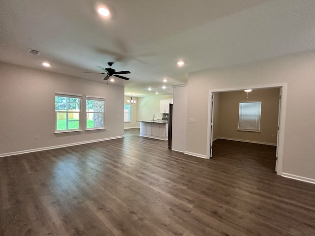 unfurnished living room featuring ceiling fan with notable chandelier and dark wood-type flooring