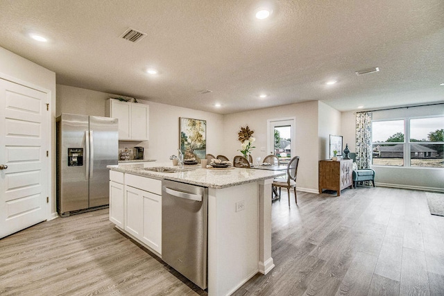 kitchen featuring white cabinetry, stainless steel appliances, a center island with sink, and plenty of natural light