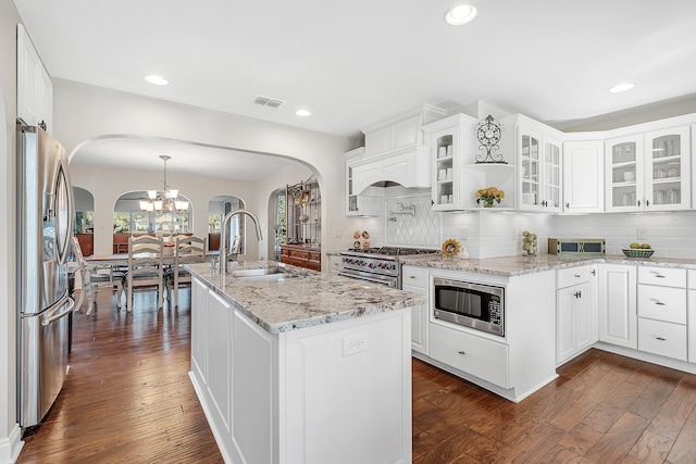 kitchen featuring white cabinetry, hanging light fixtures, a kitchen island with sink, stainless steel appliances, and light stone countertops