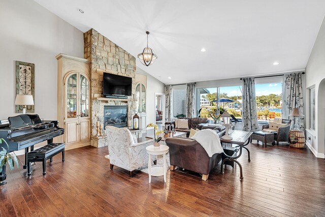 living room with an inviting chandelier, a stone fireplace, high vaulted ceiling, and dark hardwood / wood-style floors