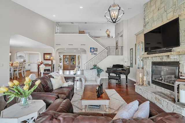 living room featuring an inviting chandelier, a stone fireplace, dark hardwood / wood-style floors, and a towering ceiling