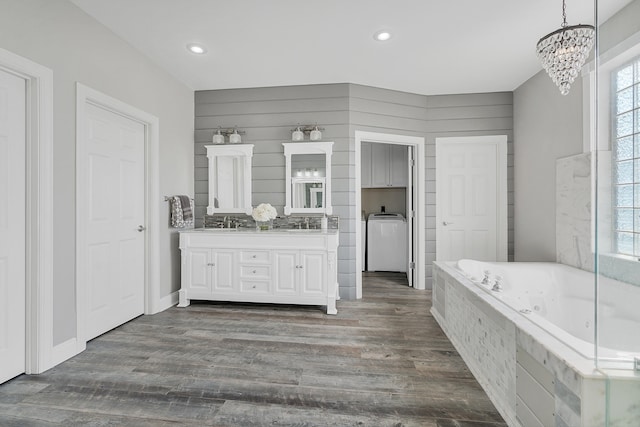 bathroom with an inviting chandelier, wood-type flooring, vanity, tiled tub, and washer / clothes dryer