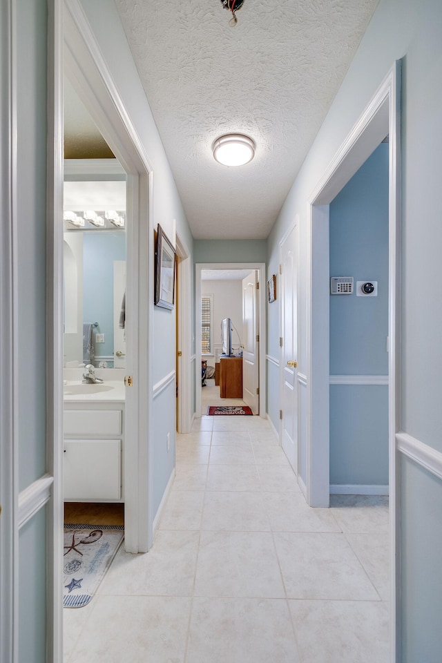 hall with sink, a textured ceiling, and light tile patterned floors