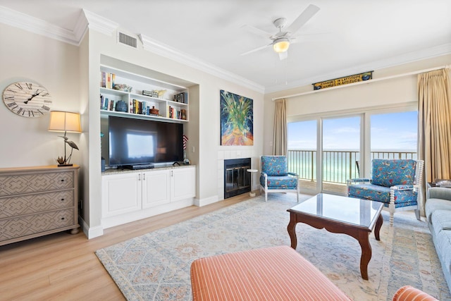 living room featuring crown molding, a tile fireplace, ceiling fan, and light wood-type flooring