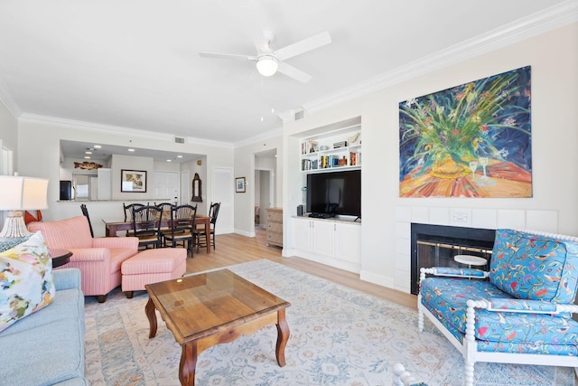 living room featuring a fireplace, built in shelves, ornamental molding, light hardwood / wood-style floors, and ceiling fan