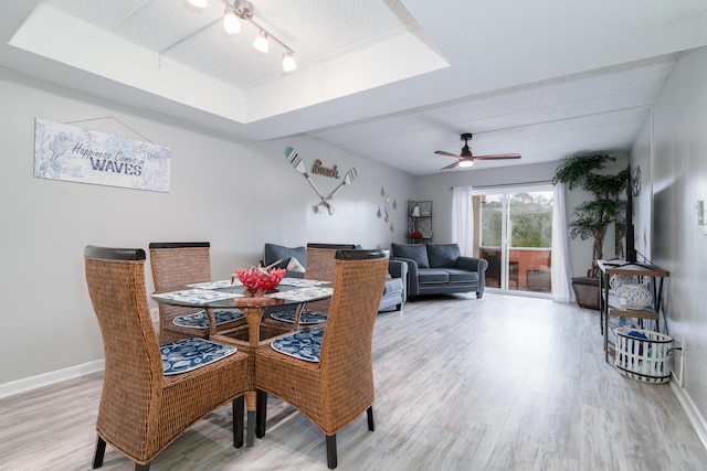 dining room featuring ceiling fan, a textured ceiling, light hardwood / wood-style floors, a raised ceiling, and rail lighting