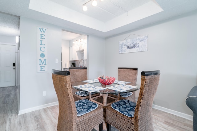 dining area with sink, light wood-type flooring, a textured ceiling, and a tray ceiling