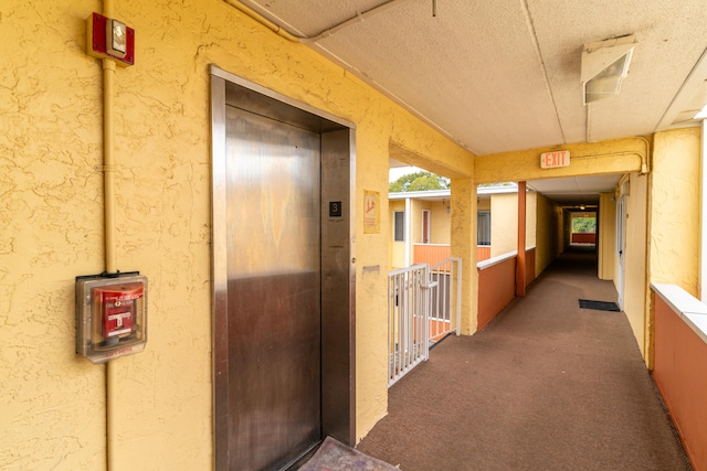 corridor with a textured ceiling, dark carpet, and elevator