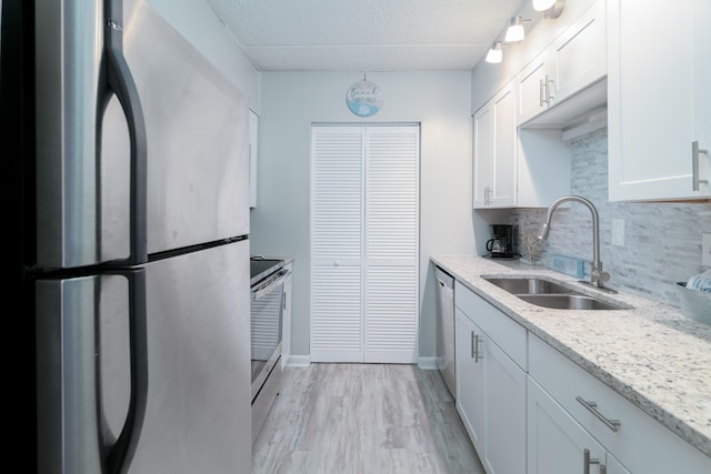 kitchen with stainless steel appliances, tasteful backsplash, white cabinetry, sink, and light wood-type flooring