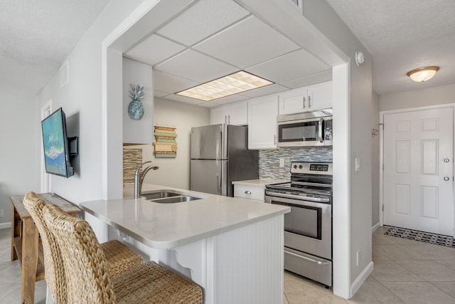 kitchen with a breakfast bar, white cabinets, stainless steel appliances, light tile floors, and tasteful backsplash