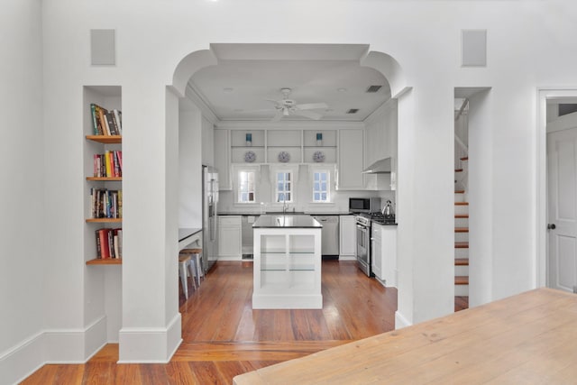 kitchen with ceiling fan, white cabinets, wall chimney range hood, stainless steel appliances, and light hardwood / wood-style flooring