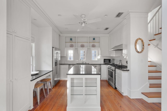 kitchen featuring a center island, appliances with stainless steel finishes, wall chimney range hood, and light hardwood / wood-style flooring