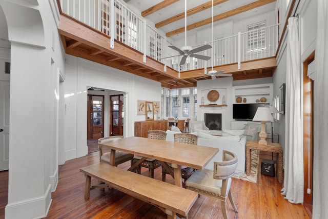 dining area with ceiling fan, a towering ceiling, a fireplace, light wood-type flooring, and built in features