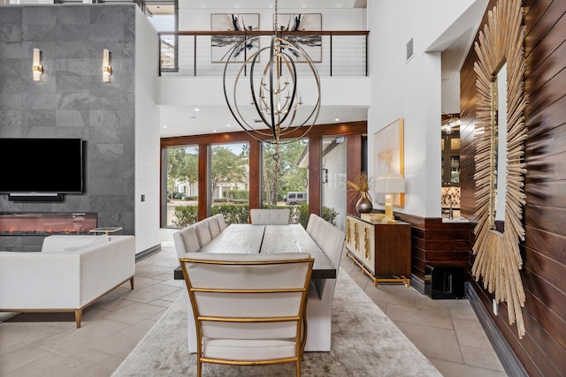 dining area featuring tile walls, a tiled fireplace, a high ceiling, an inviting chandelier, and light tile floors