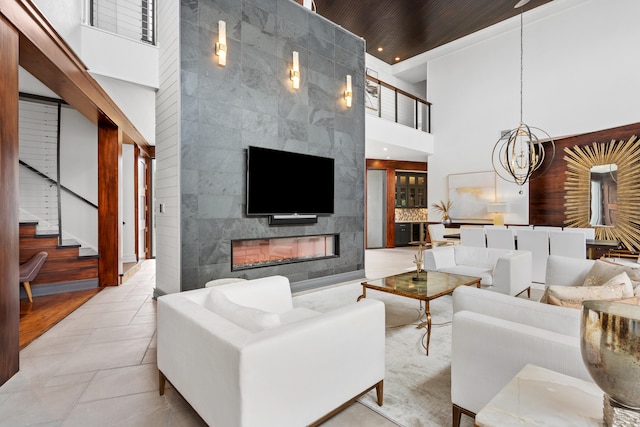 living room featuring an inviting chandelier, tile walls, a towering ceiling, and a tiled fireplace