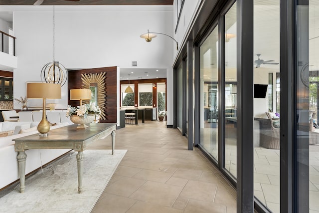 corridor featuring a chandelier, a towering ceiling, light tile floors, and a wealth of natural light