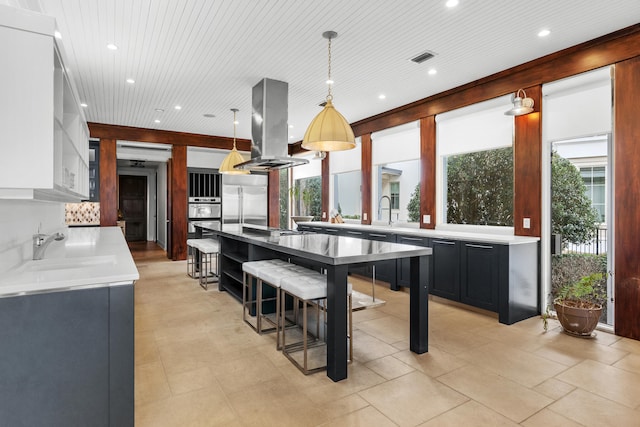 kitchen with a healthy amount of sunlight, pendant lighting, island exhaust hood, and a kitchen bar