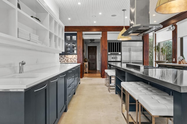 kitchen featuring hanging light fixtures, island range hood, stainless steel appliances, sink, and tasteful backsplash