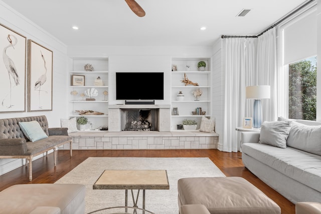 living room with ceiling fan, dark wood-type flooring, built in shelves, and ornamental molding