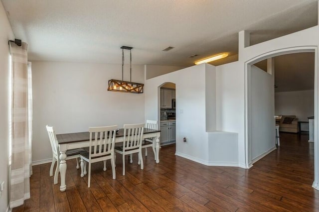 dining room featuring a textured ceiling, dark wood-type flooring, and vaulted ceiling