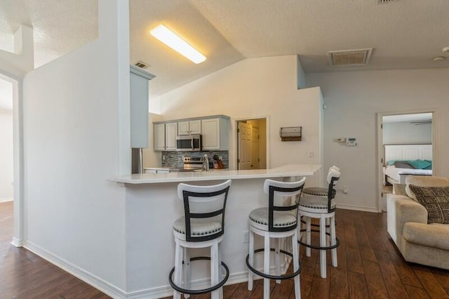 kitchen featuring kitchen peninsula, appliances with stainless steel finishes, dark hardwood / wood-style flooring, vaulted ceiling, and a breakfast bar area